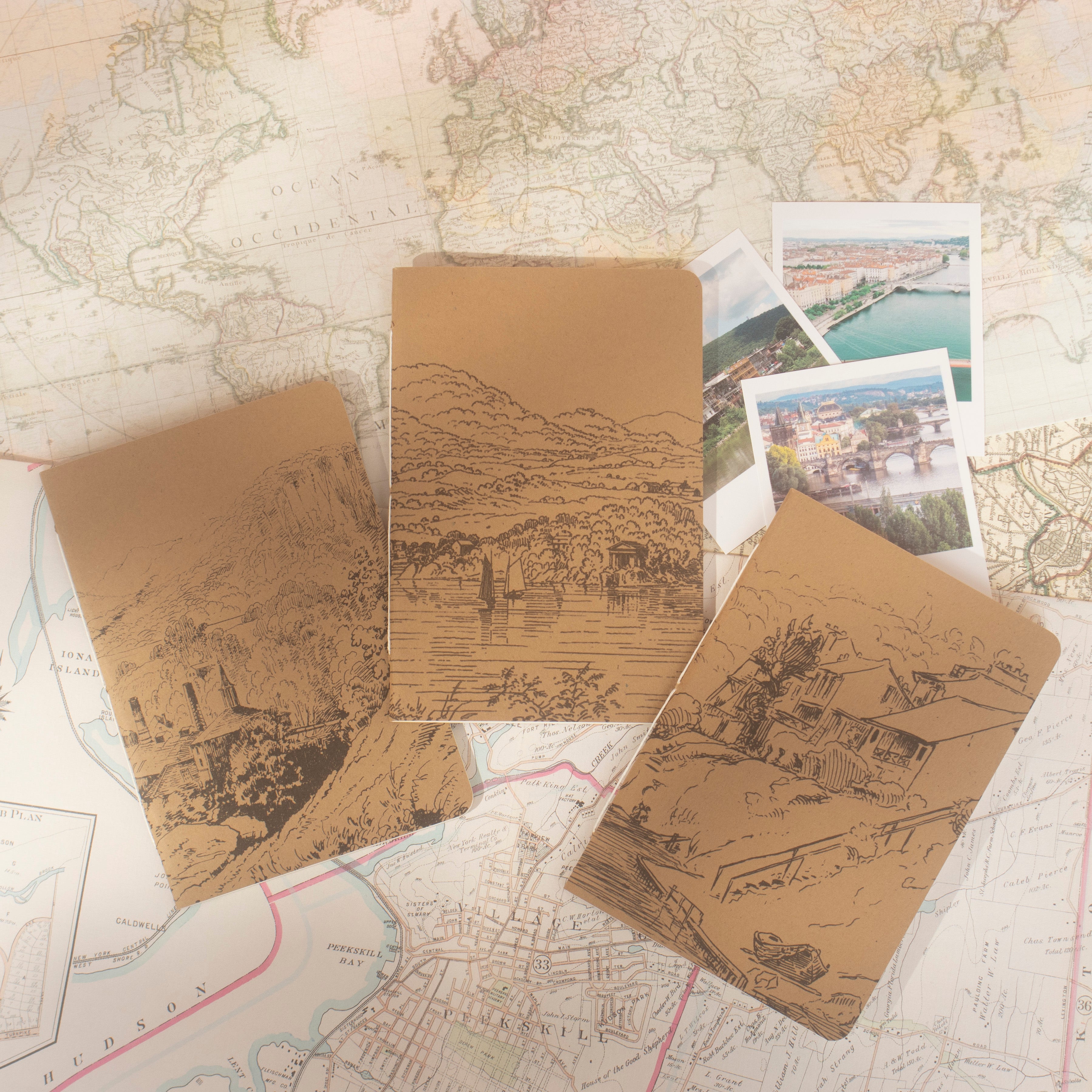 Front of three kraft notebooks with illustrations of towns and villages on vintage maps. 