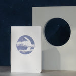 Notebook with a moon illustration on the cover against a starry night sky.