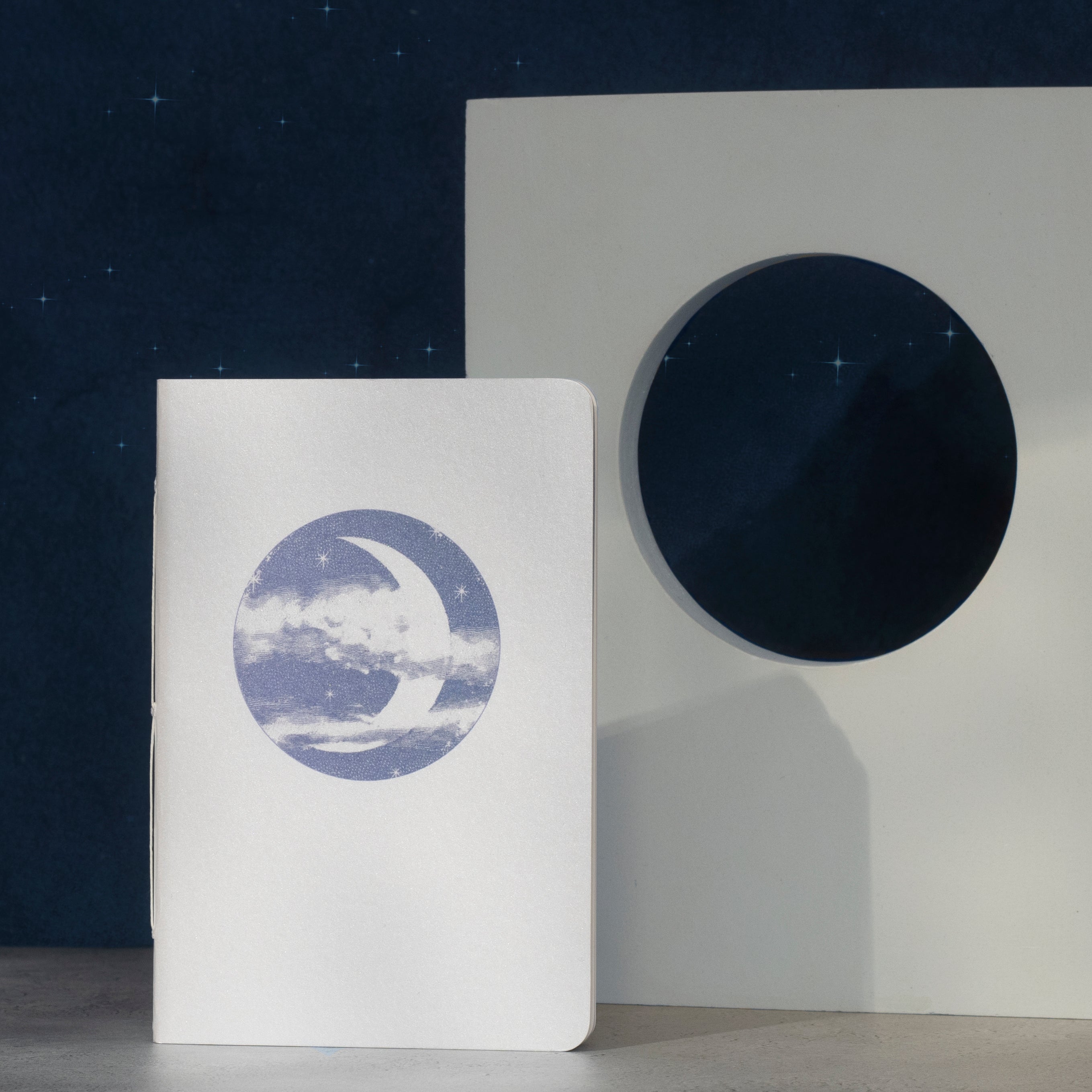 Notebook with a moon illustration on the cover against a starry night sky.