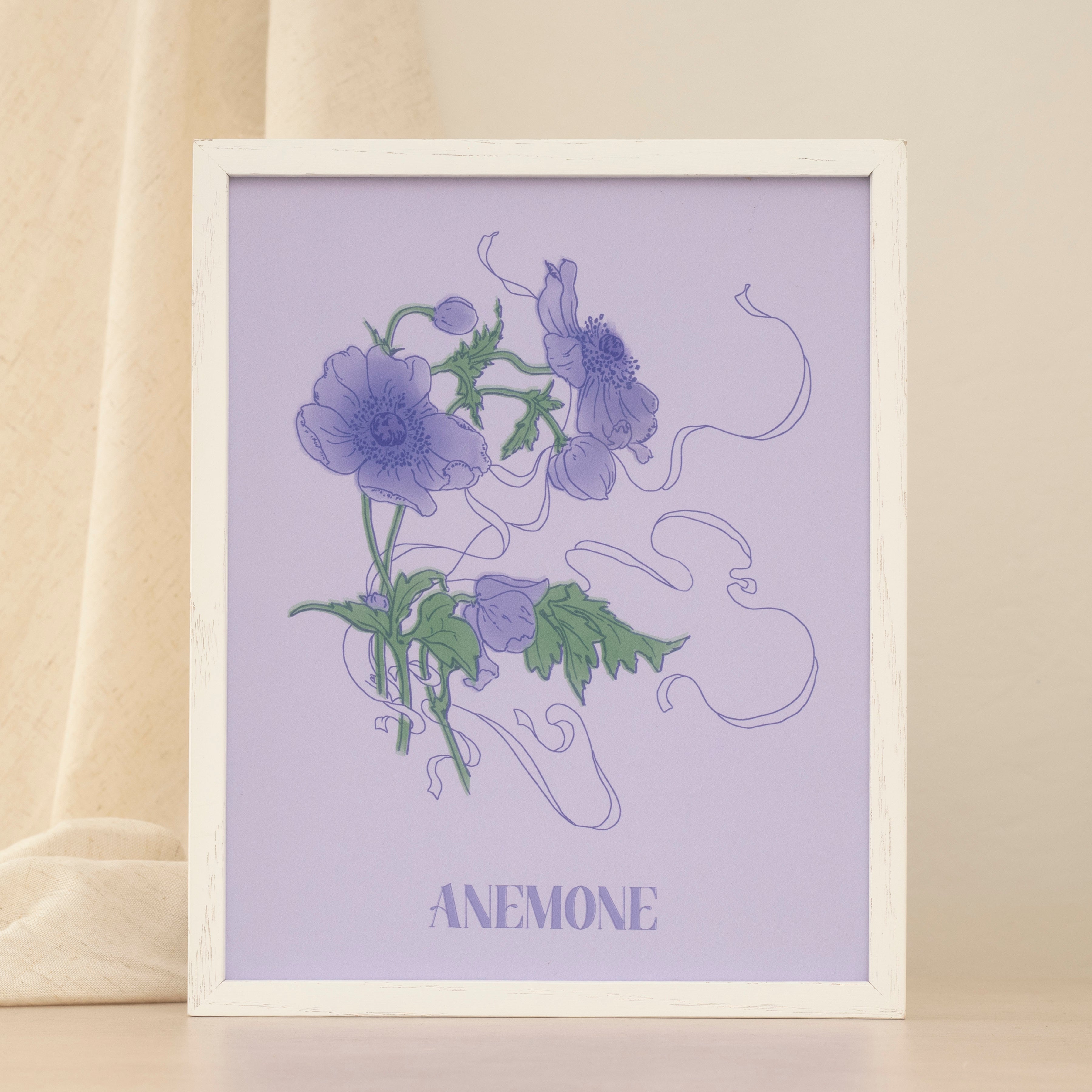 Framed artwork of purple anemone flowers on a light purple background with text 'ANEMONE' on a neutral backdrop.