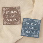 Brown and blue 'Patron of Small Shops' stickers on a textured fabric background. 