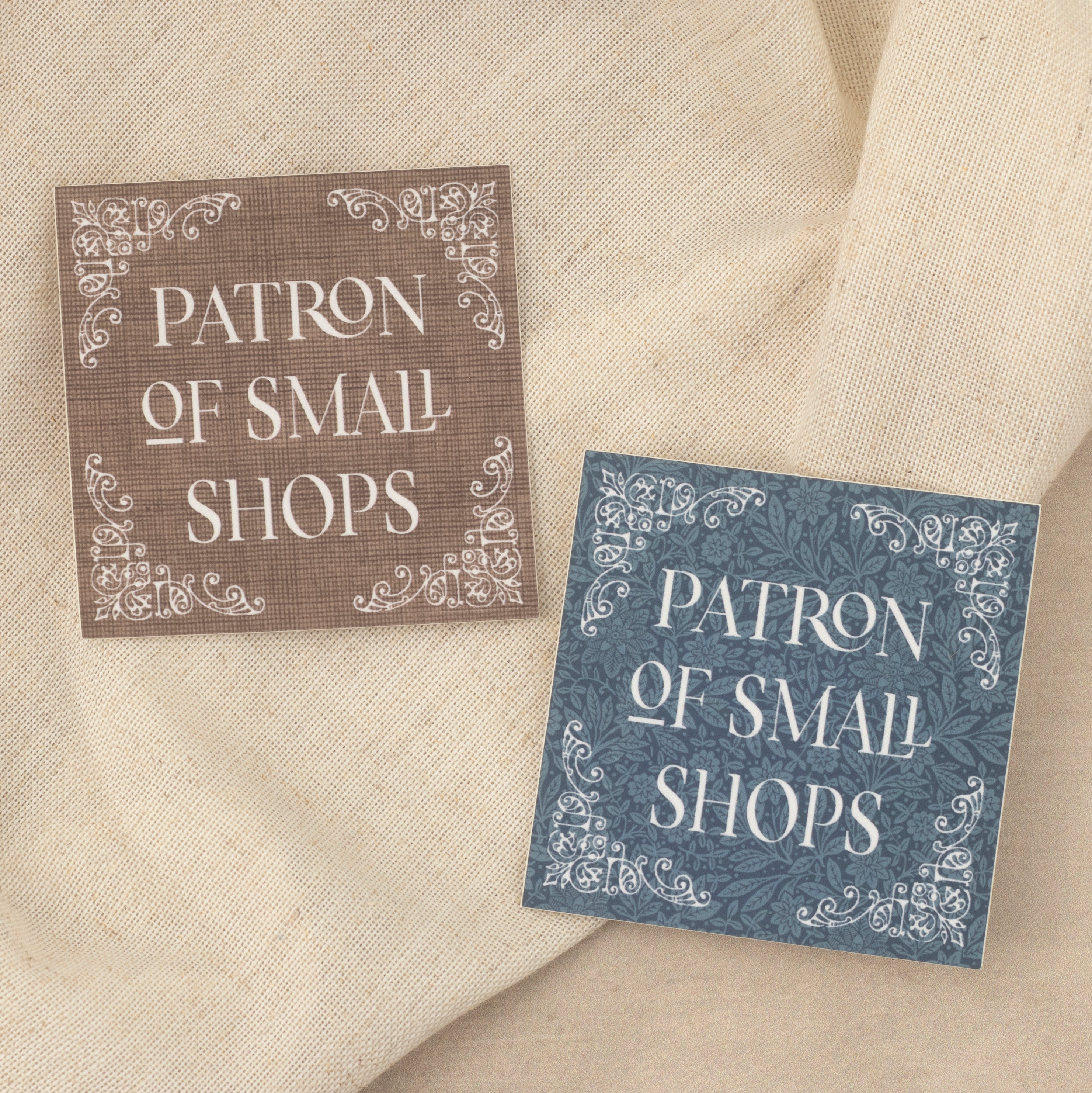 Brown and blue 'Patron of Small Shops' stickers on a textured fabric background. 