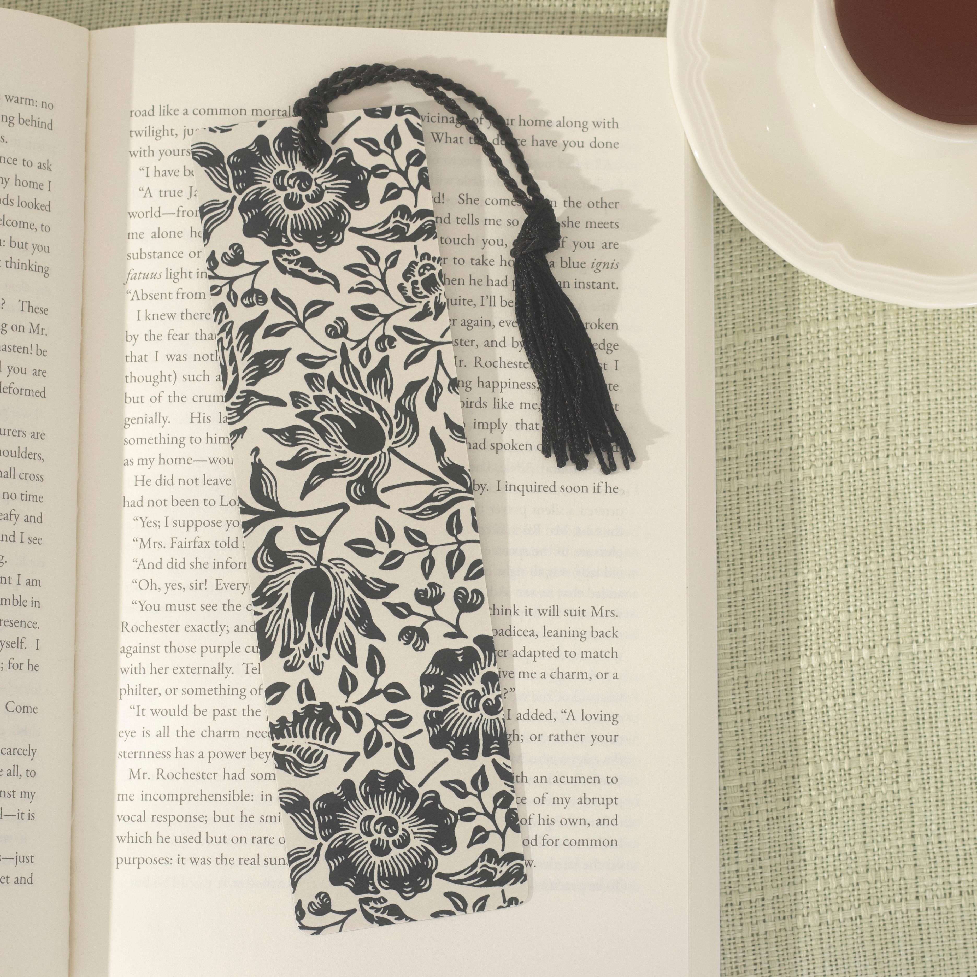 Front of a floral black and white cream bookmark with a black tassel on an open book.