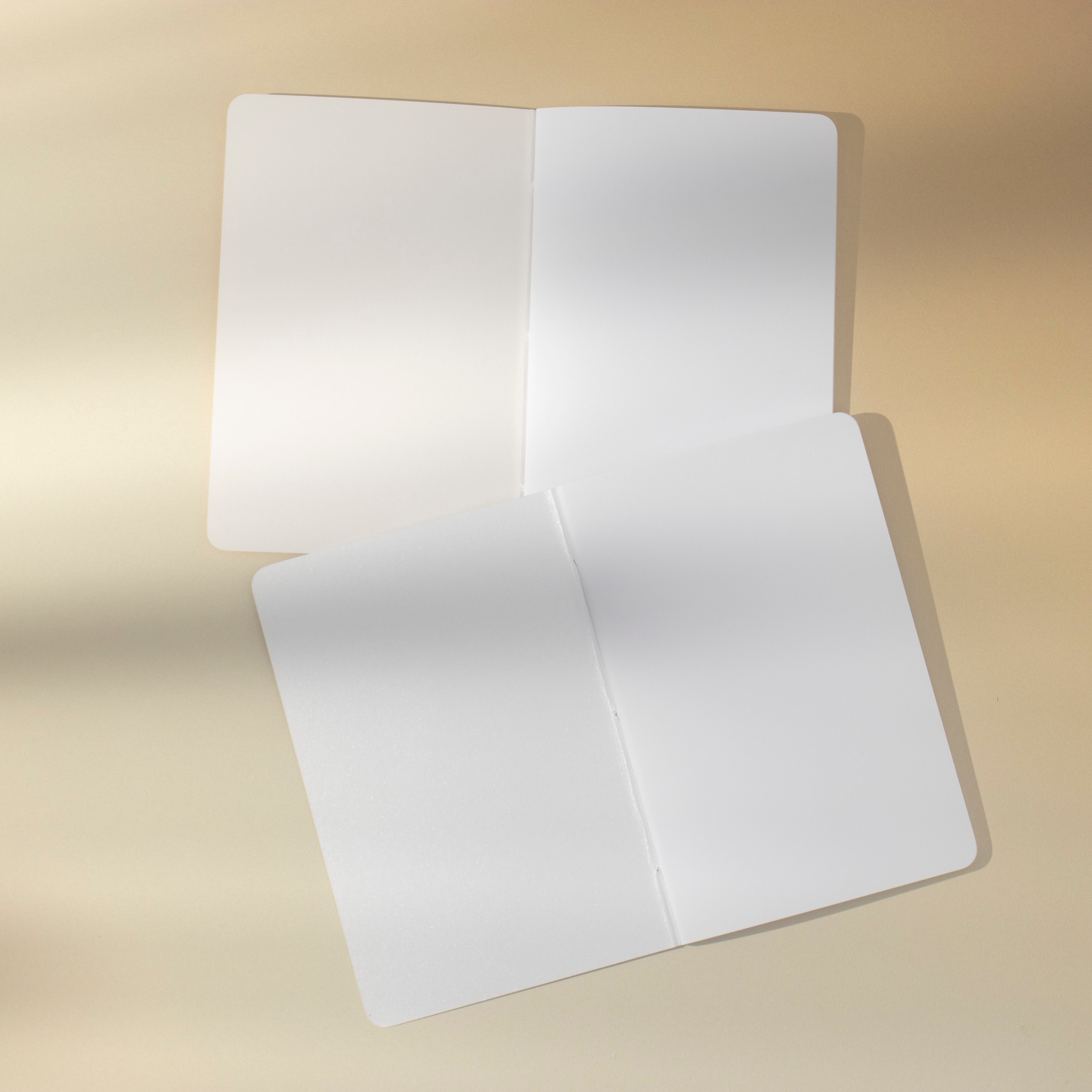 Two open notebooks with blank white pages on a beige background.