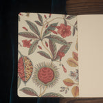 An open botanical-patterned notebook with blank natural white paper on dark wood.