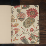 An open botanical-patterned notebook with blank natural white paper on dark wood.