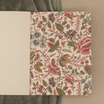 An open floral-patterned notebook with natural white blank paper on a green and beige background.