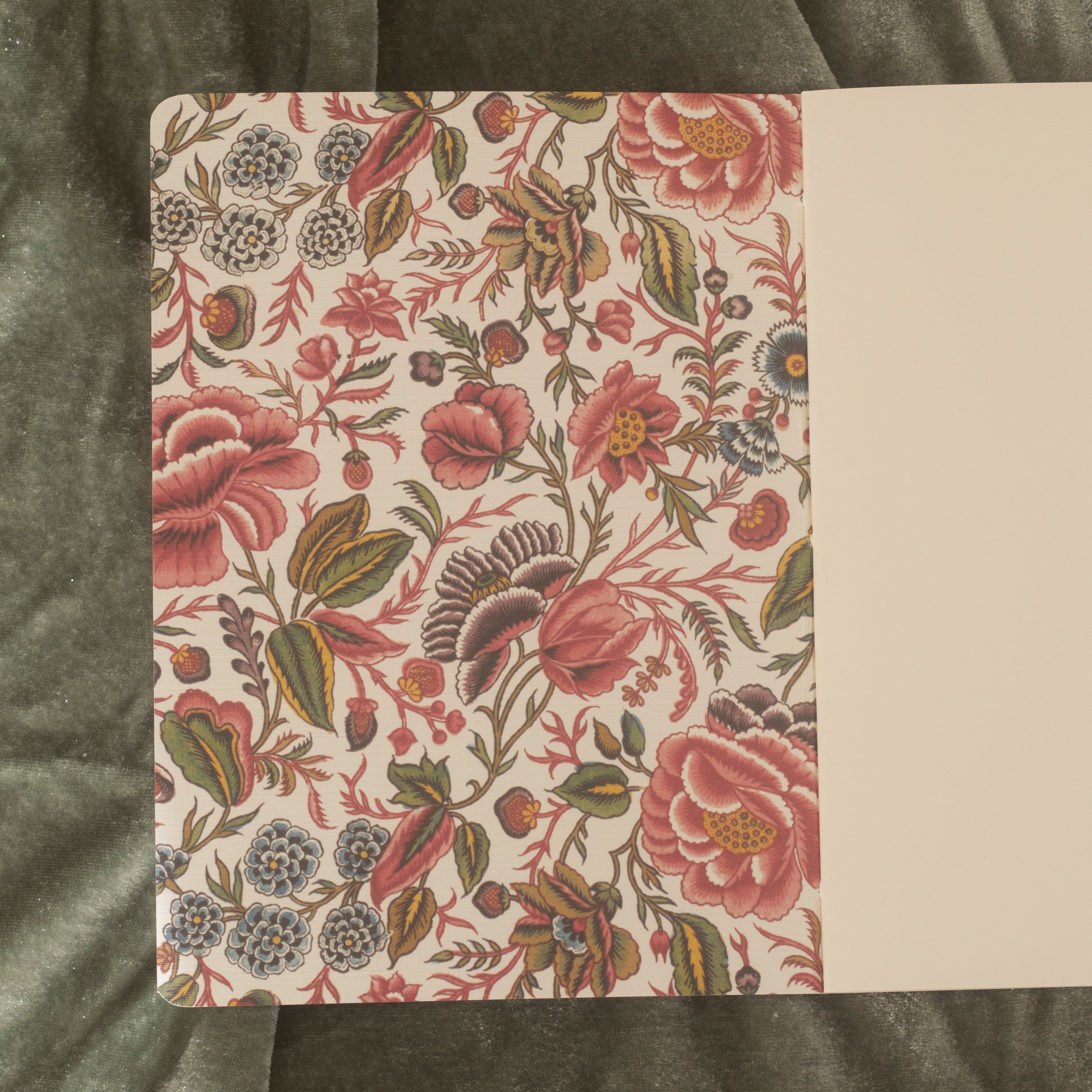 An open floral-patterned notebook with natural white blank paper on a green background.