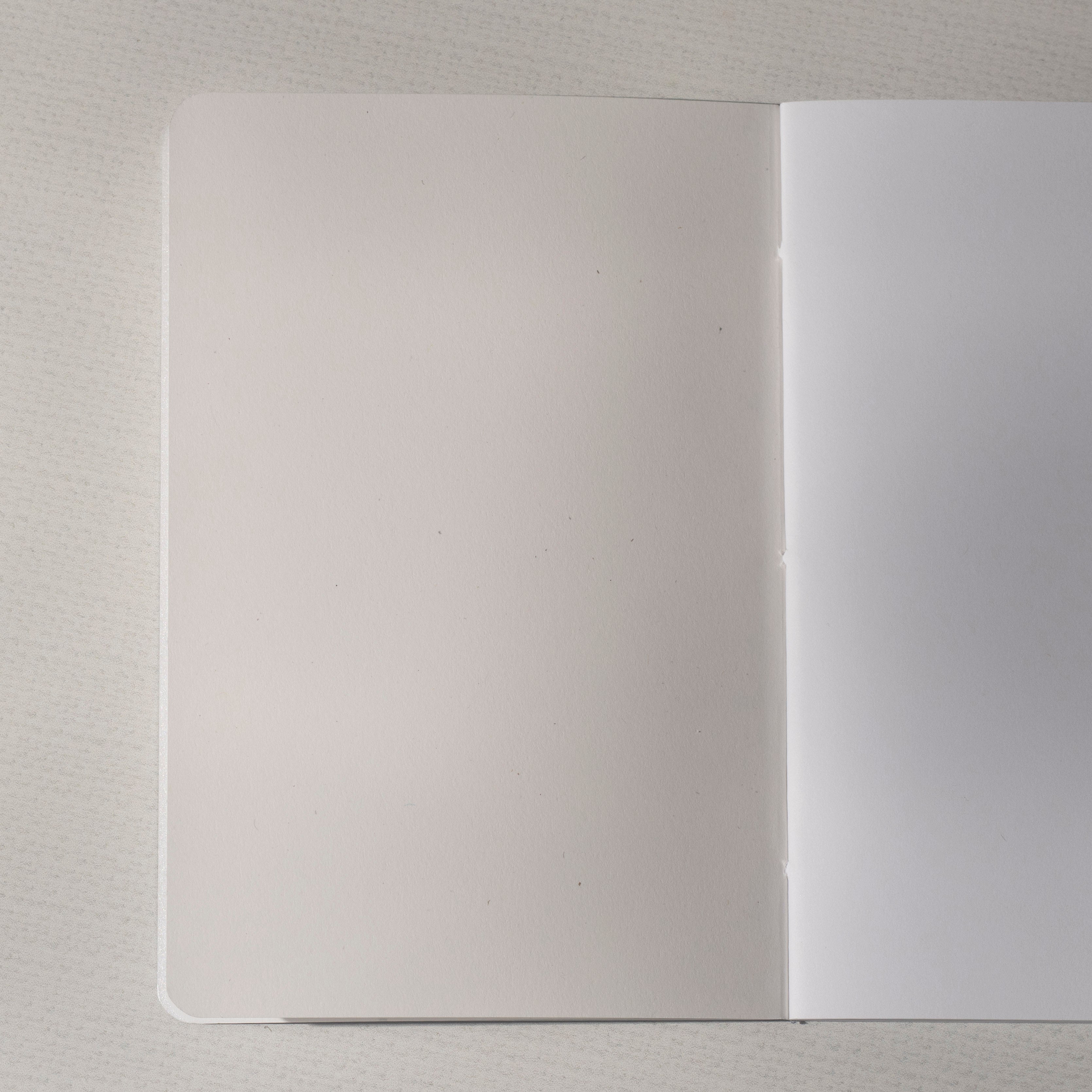 A blank notebook with one blank off-white and white page, shown open on a light gray textured surface.