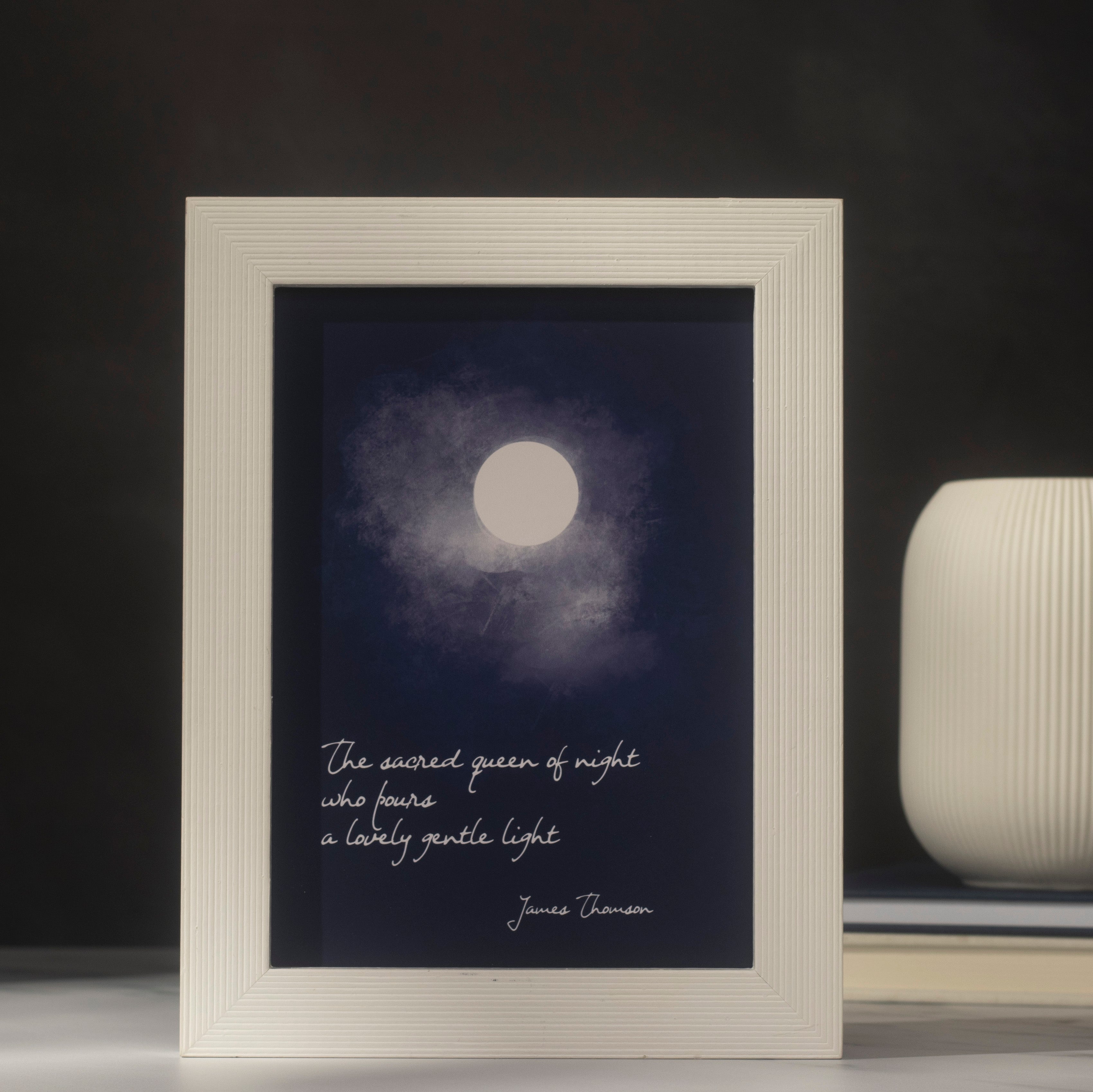 Framed artwork with a moon illustration and text on a dark background. The quote reads, "The sacred queen of night. Who pours a lovely gentle light," and the text James Thomson " is on the lower right.
