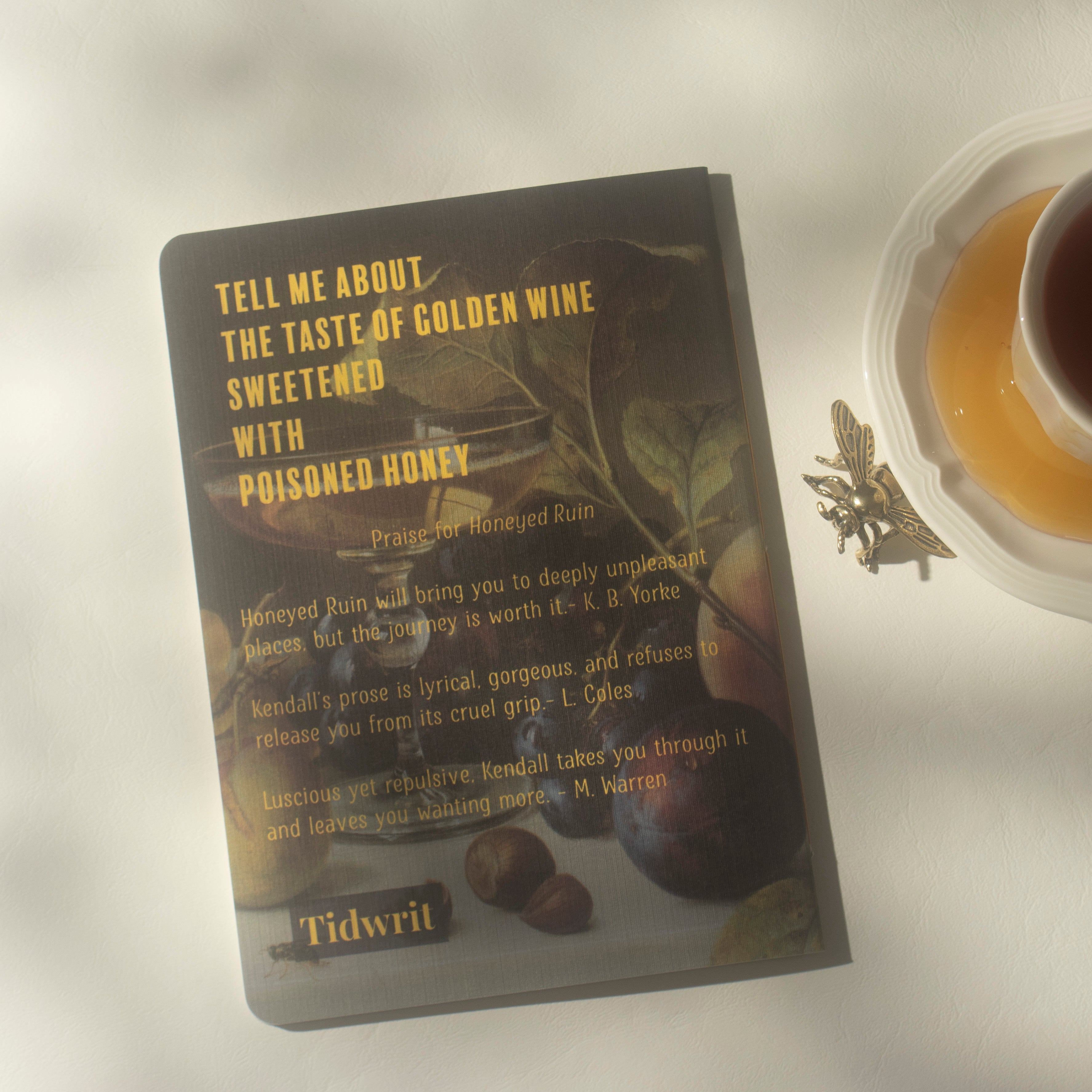 A notebook with a still life featuring yellow text on a light surface, next to a cup of tea and a decorative bee figurine.